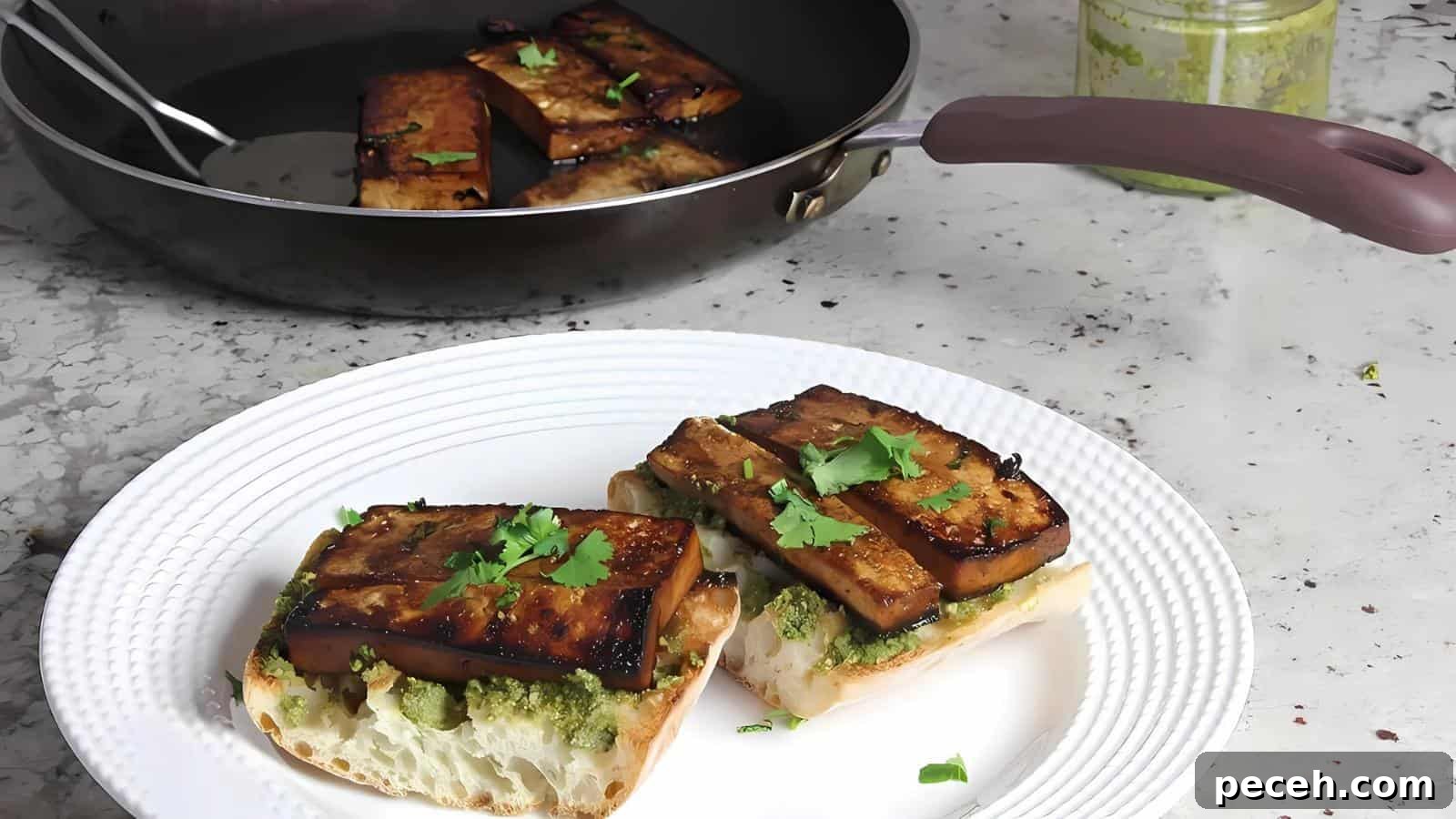 Tofu sandwiches with green pesto and cilantro on a white plate, next to a pan with more tofu pieces.