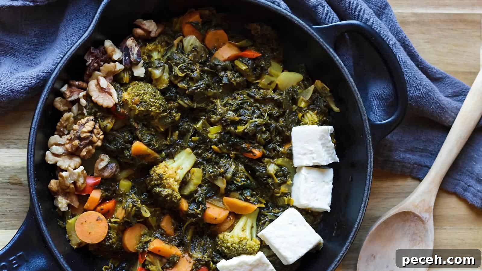 A black skillet filled with cooked vegetables such as broccoli, carrots, and greens, along with walnuts and slices of cheese, placed on a wooden surface with a wooden spoon nearby.