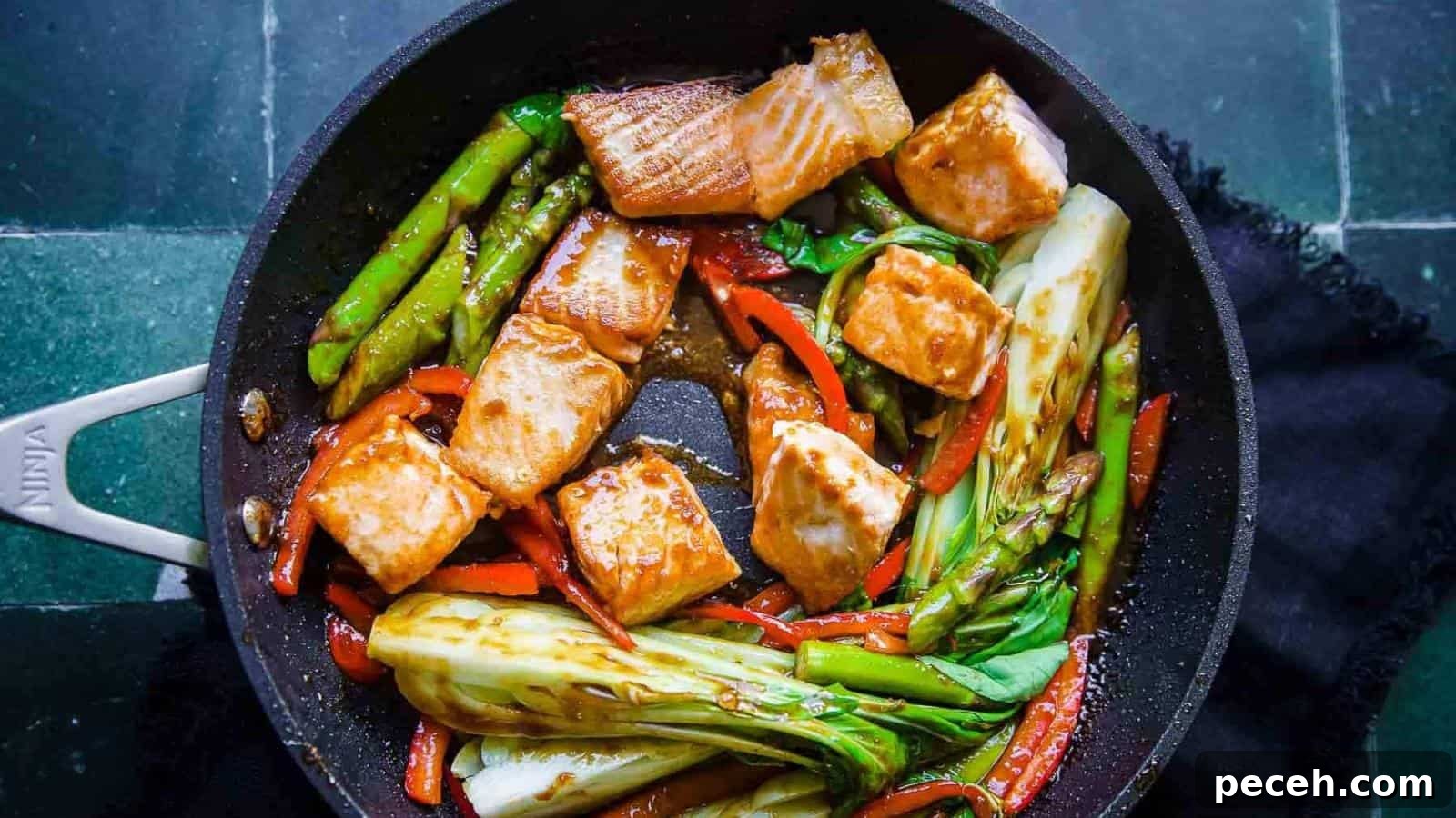 A pan with cooked salmon pieces, asparagus, bok choy, and red bell peppers in a sauce.