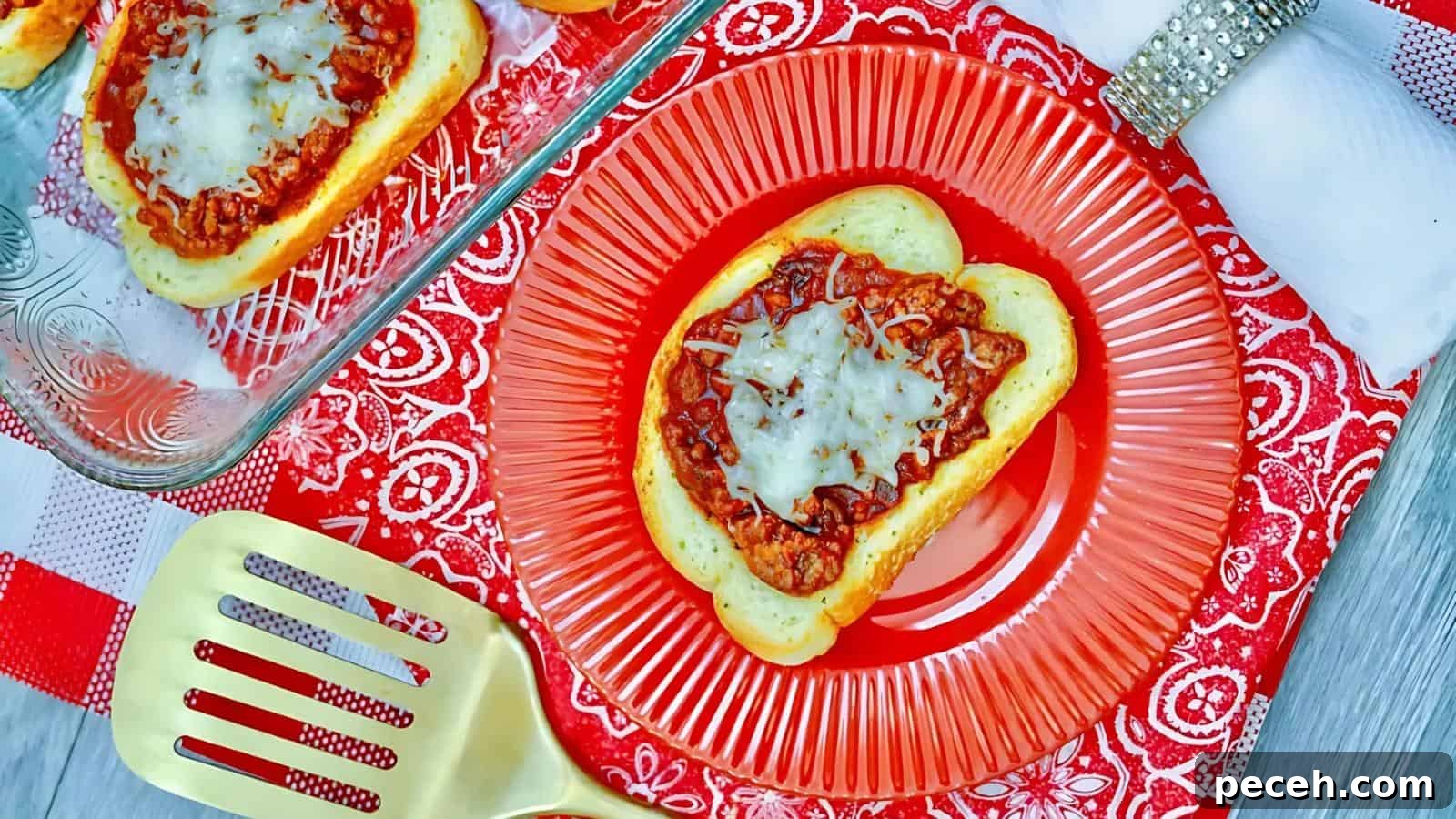 Bread slices topped with tomato sauce and melted cheese on a red plate, placed on a red patterned tablecloth. A spatula and a napkin with a silver ring are also visible.