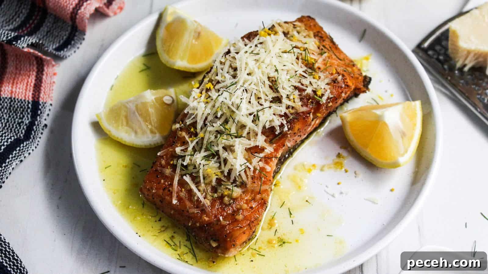 Grilled salmon fillet garnished with lemon slices and grated cheese on a white plate, accompanied by a red and white striped napkin.