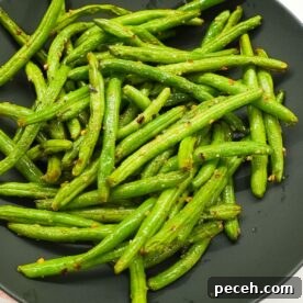 Air fryer green beans in a bowl with visible garlic, red pepper flakes, and lightly blistered edges.