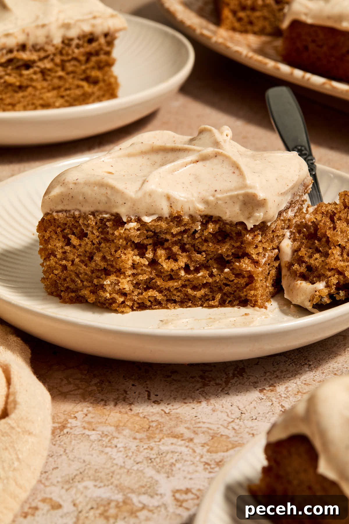 Vegan Chai-Spiced Layer Cake Recipe 2 A piece of chai cake on a plate with a forkful removed and other pieces on plates in the background.