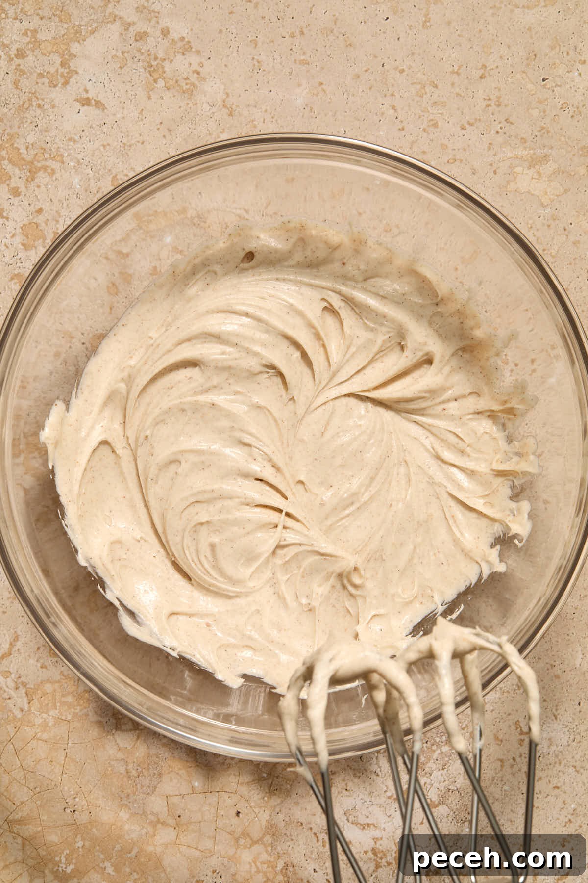 Vegan Chai-Spiced Layer Cake Recipe 11 Frosting whipped together in a glass bowl with beaters in the frame.