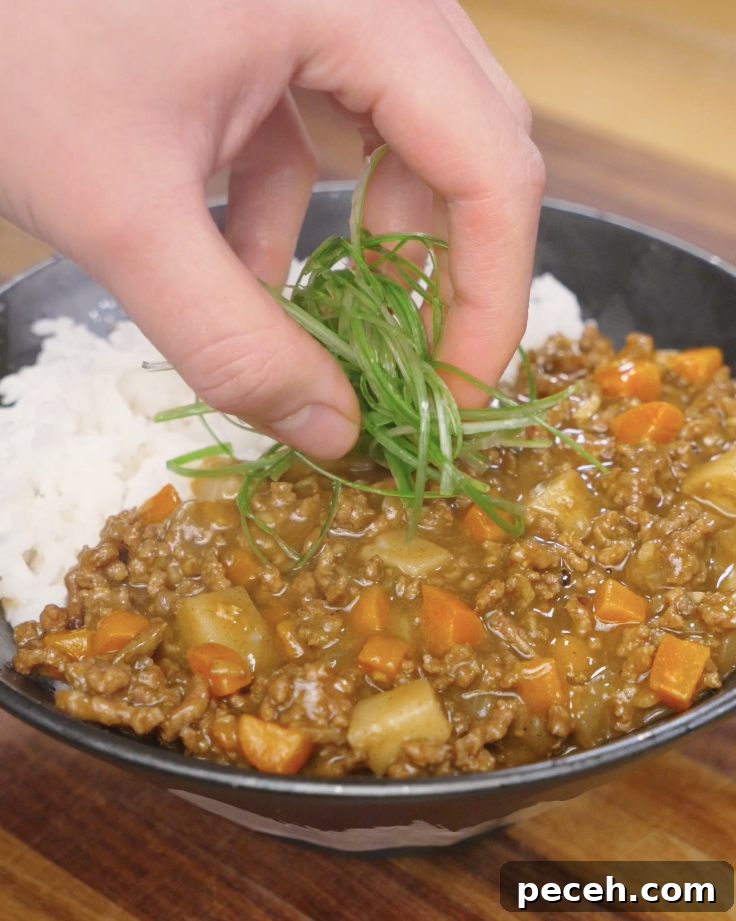 Freshly sliced scallions being added on top of Japanese ground beef curry served with rice for a final garnish.