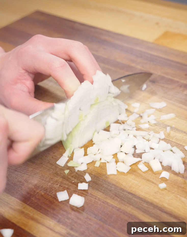 Finely diced onion being chopped on a wooden cutting board as the base aromatics for an easy Japanese ground beef curry recipe.