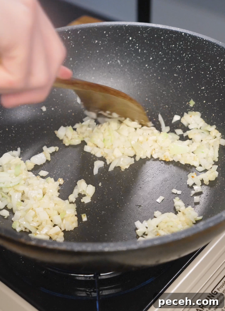Finely diced onion being sautéed in a nonstick pan until softened, forming the aromatic base for a quick Japanese ground beef curry.