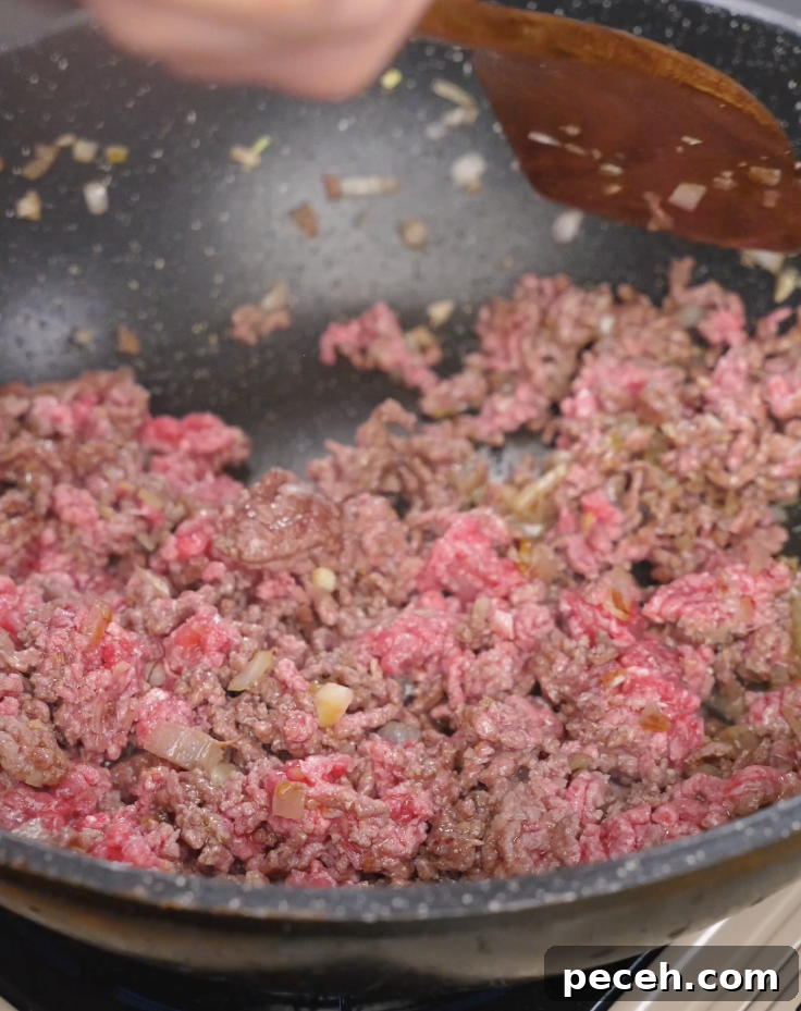 Ground beef cooking in a pan with sautéed onions, partially browned and broken apart for an easy weeknight Japanese curry.