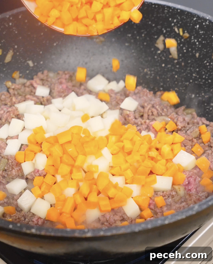 Diced potatoes and carrots being added to browned ground beef in a pan, preparing the vegetable base for Japanese ground beef curry.