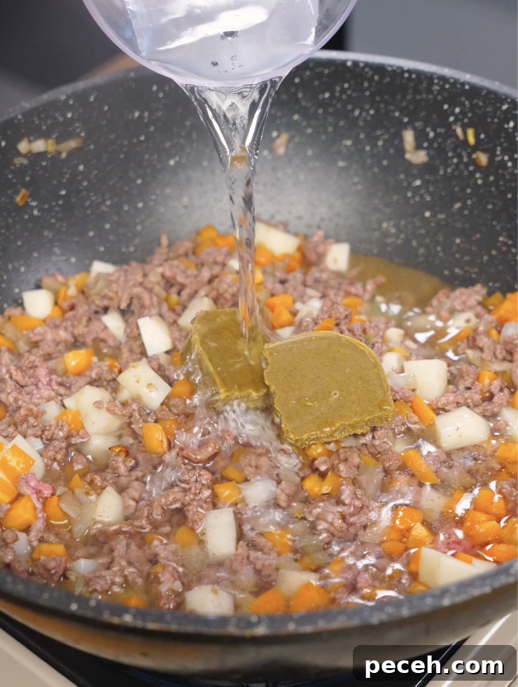 Water being poured into the pan with ground beef, vegetables, and Japanese curry blocks as the sauce begins to form.