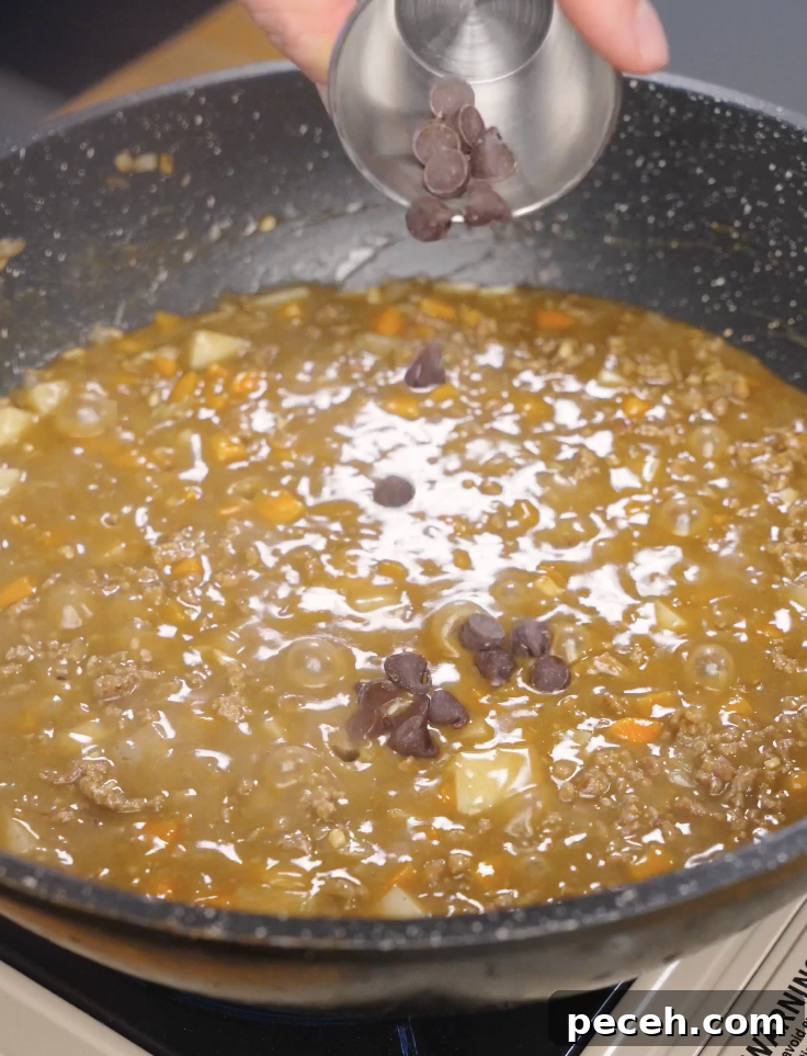 Dark chocolate being added to simmering Japanese ground beef curry to deepen flavor and add richness to the sauce.