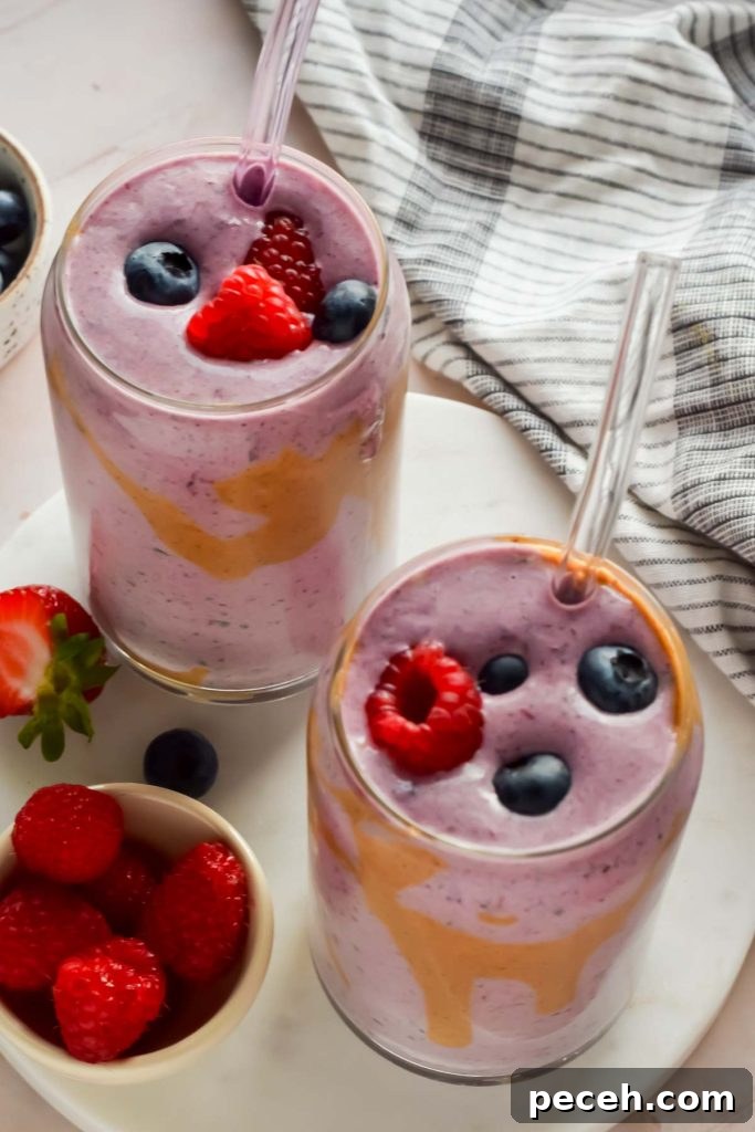 Mango Spinach Smoothie Recipe for Energy and Glow 8 two berry smoothies in clear glasses with glass straws topped with fresh raspberries and blueberries.