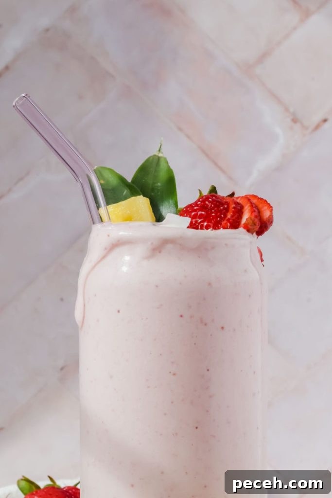 Mango Spinach Smoothie Recipe for Energy and Glow 10 tropical smoothie bahama mama in clear glass with straw garnished with strawberry slices and pineapple.