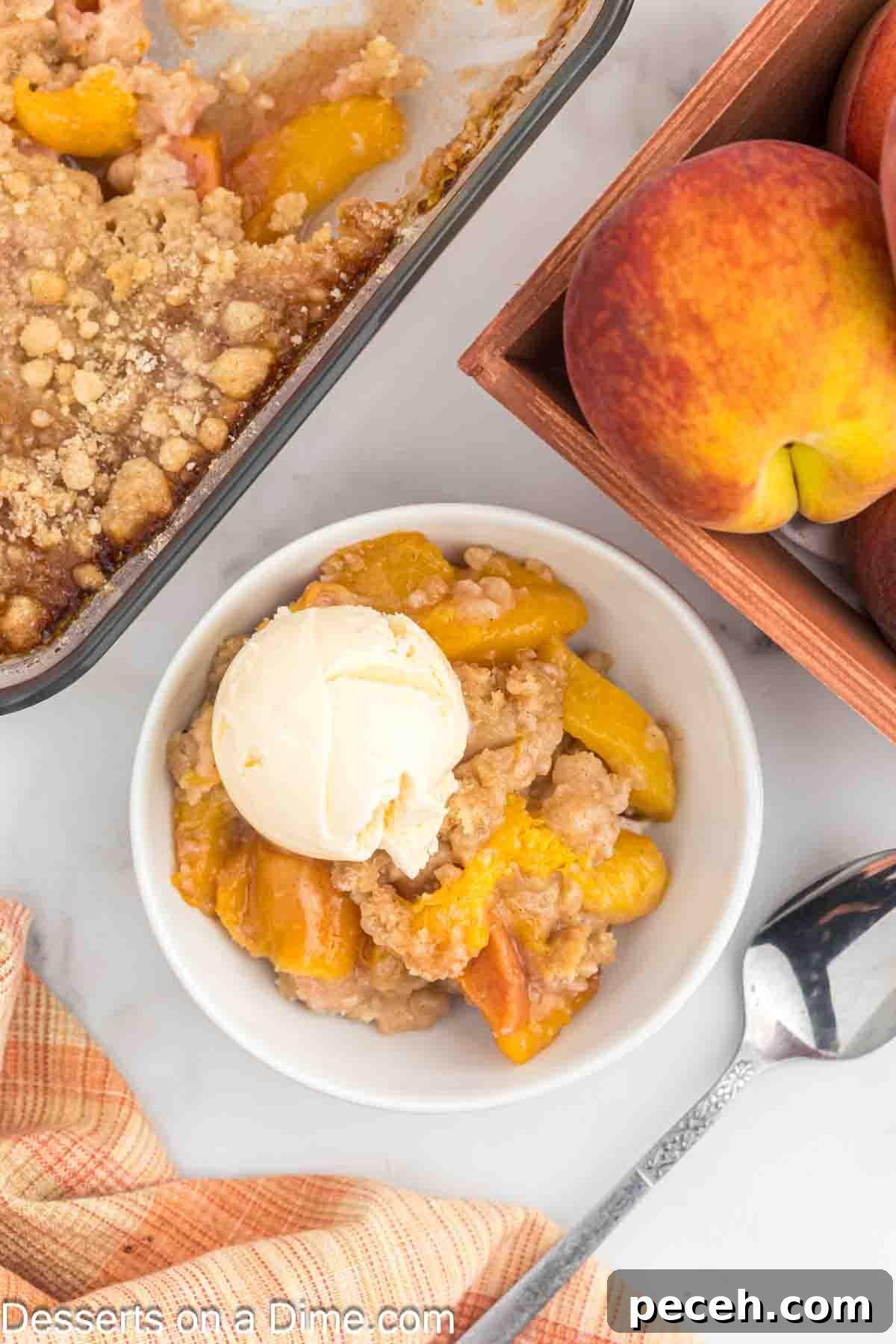 Perfect Peach Crumble Recipe for Summer Desserts 10 Overview of peach crumble in a small bowl topped with ice cream with apples and the pan behind it.