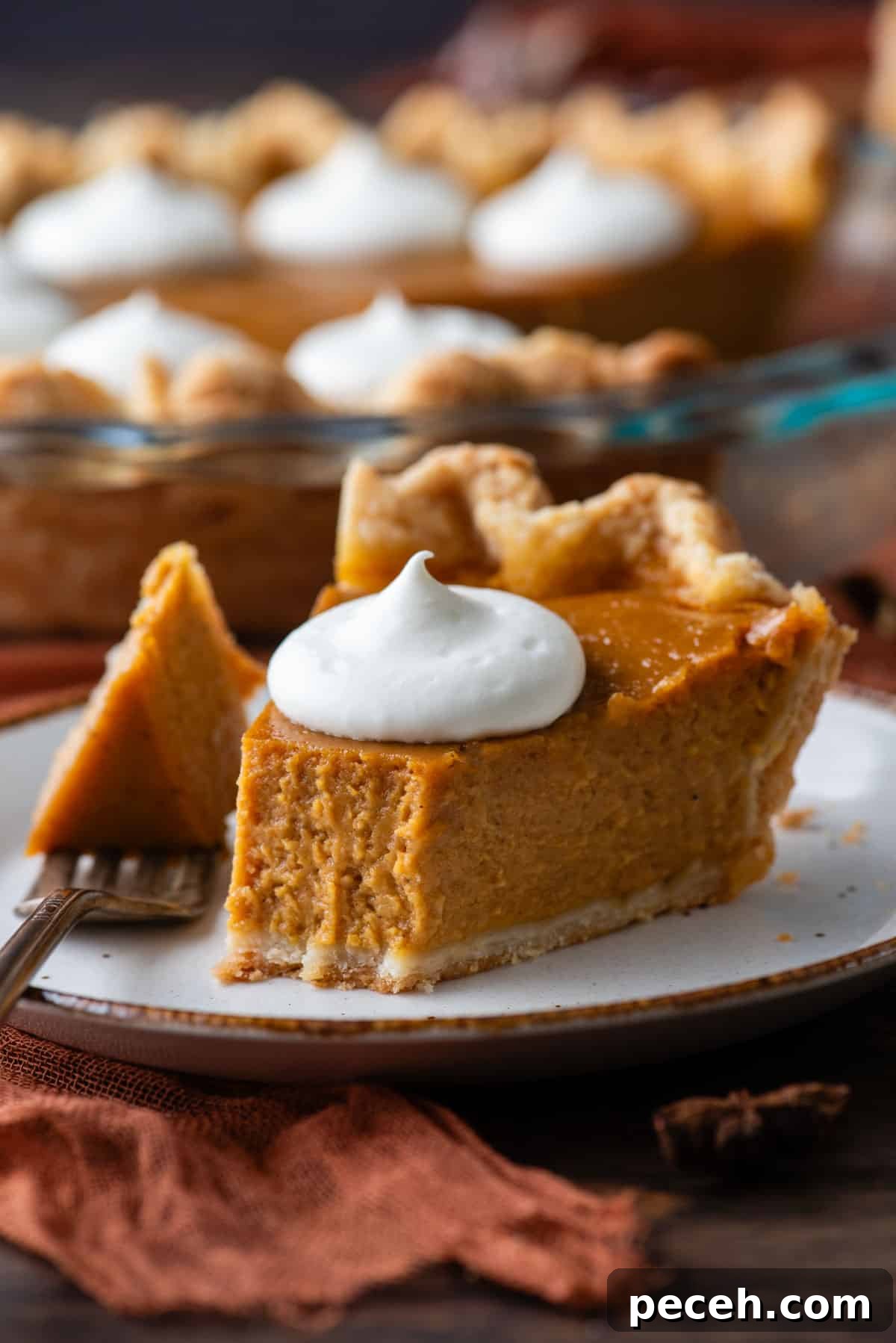 Classic Homemade Pumpkin Pie: Simple Recipe for Perfect Fall Dessert 3 a slice of pumpkin pie on a white plate topped with a dollop of whipped cream, with a fork that has taken one bite out laying on the plate beside it, and the pie dish with the rest of the pie in the background