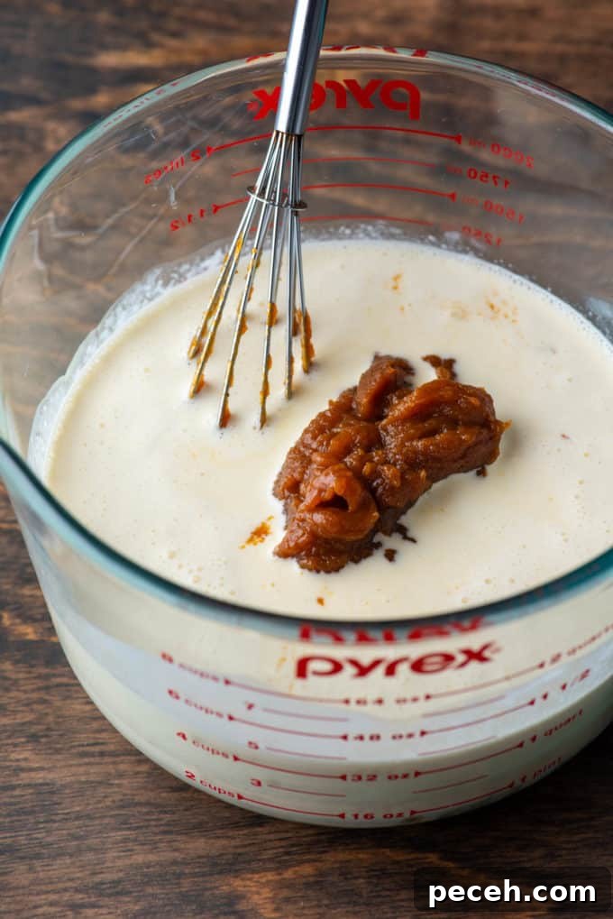 Classic Homemade Pumpkin Pie: Simple Recipe for Perfect Fall Dessert 6 pumpkin puree in a measuring cup with heavy whipping cream and a whisk, sitting on a wood surface