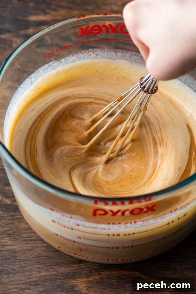 Classic Homemade Pumpkin Pie: Simple Recipe for Perfect Fall Dessert 7 pumpkin puree being mixed into heavy cream and other ingredients for pumpkin pie with a whisk in a measuring bowl