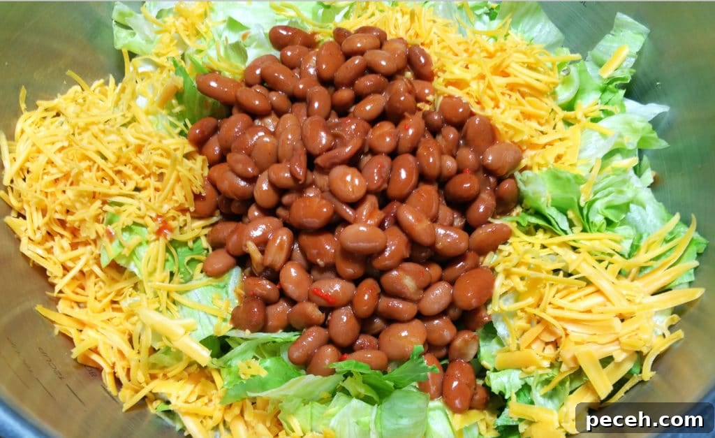 A close up of beans, shredded cheese, on a bed of chopped iceberg lettuce.