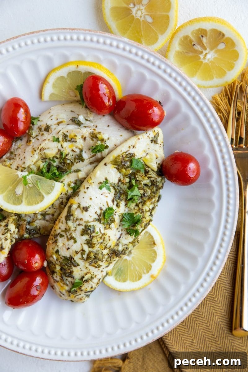 Greek Lemon and Oregano Chicken Breasts 2 Two chicken breasts on a white plate with cherry tomatoes, sliced lemons and golden napkin