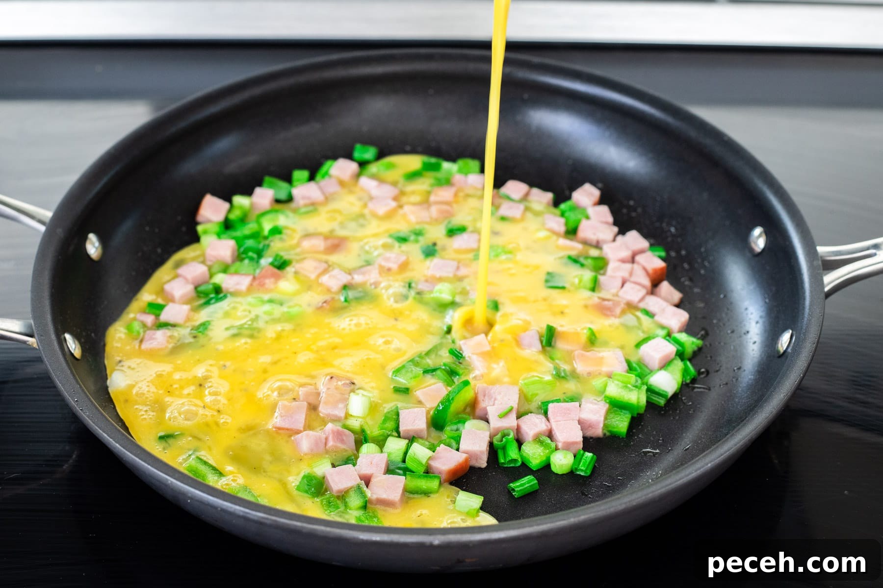 Classic Western Omelette Sandwich Recipe: How to Make It at Home 5 Pouring beaten egg over sautéed ham and veggies.