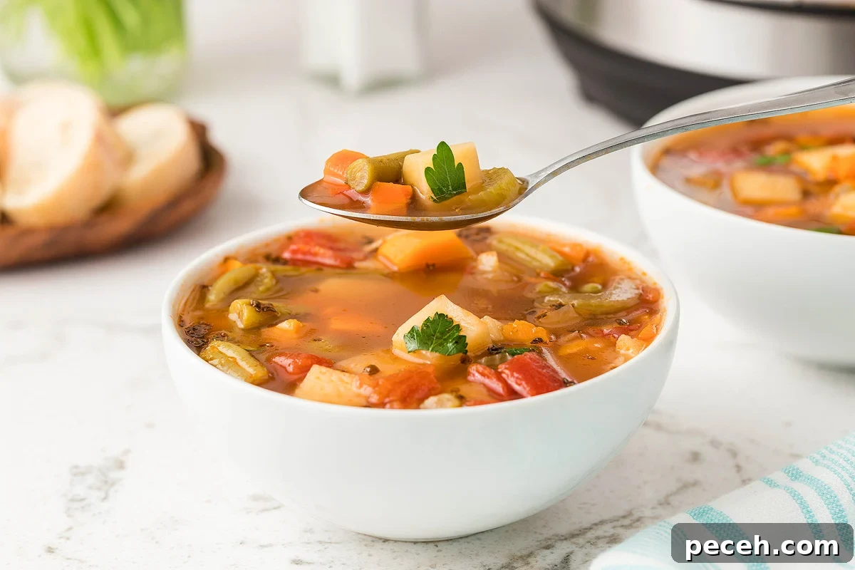 A spoon taking a scoop of vegetable soup out of a white bowl.