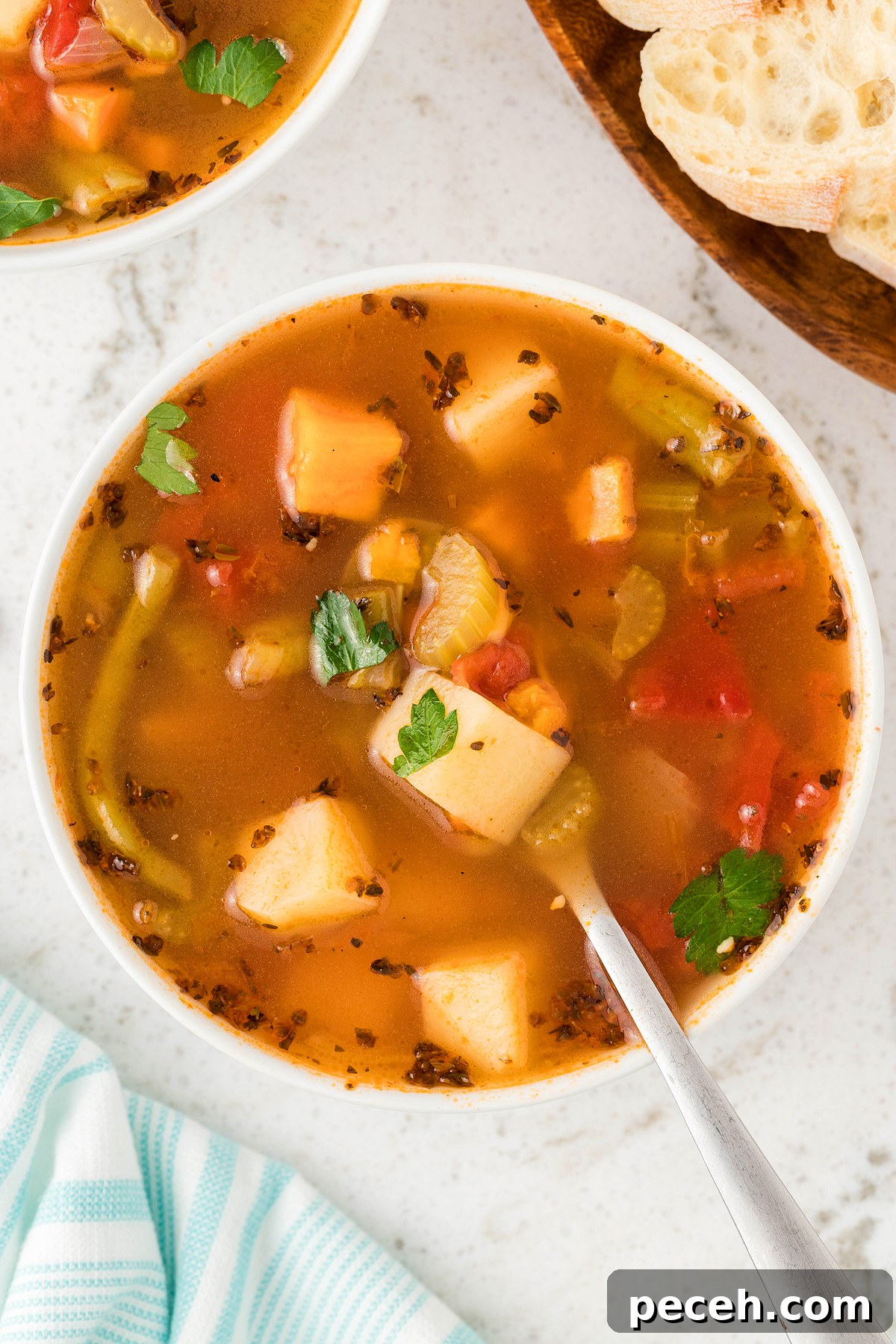 Bowl of Instant Pot Vegetable Soup with potatoes, celery, and parsley, made with fresh and frozen vegetables, next to sliced bread on a white surface.