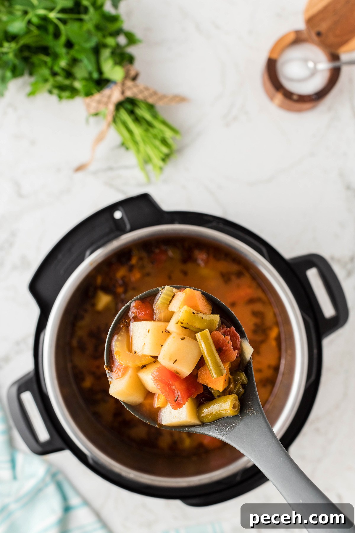 A ladle of vegetable soup above an Instant Pot, made with fresh and frozen vegetables, with fresh herbs and salt nearby on a marble countertop.