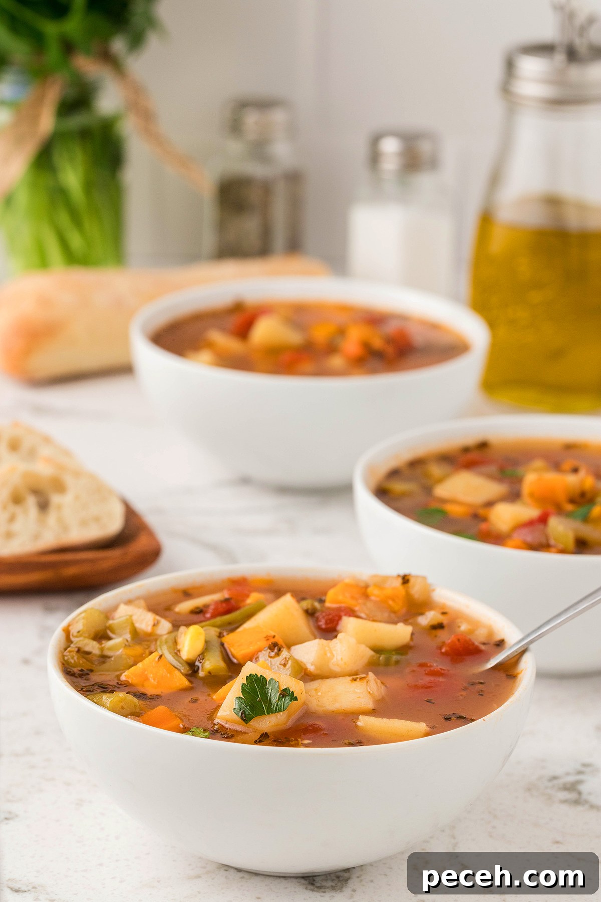 Three bowls of Instant Pot Vegetable Soup with bread rest on a white bowl, surrounded by olive oil and spices—an easy vegetarian or vegan soup recipe using fresh and frozen vegetables.