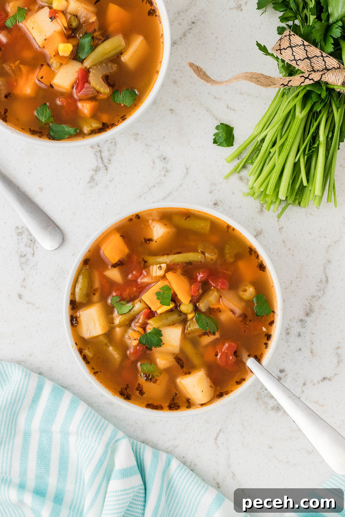 Two bowls of Instant Pot Vegetable Soup on a white surface with fresh parsley and a striped kitchen towel nearby, perfect for anyone seeking an easy vegan soup recipe.