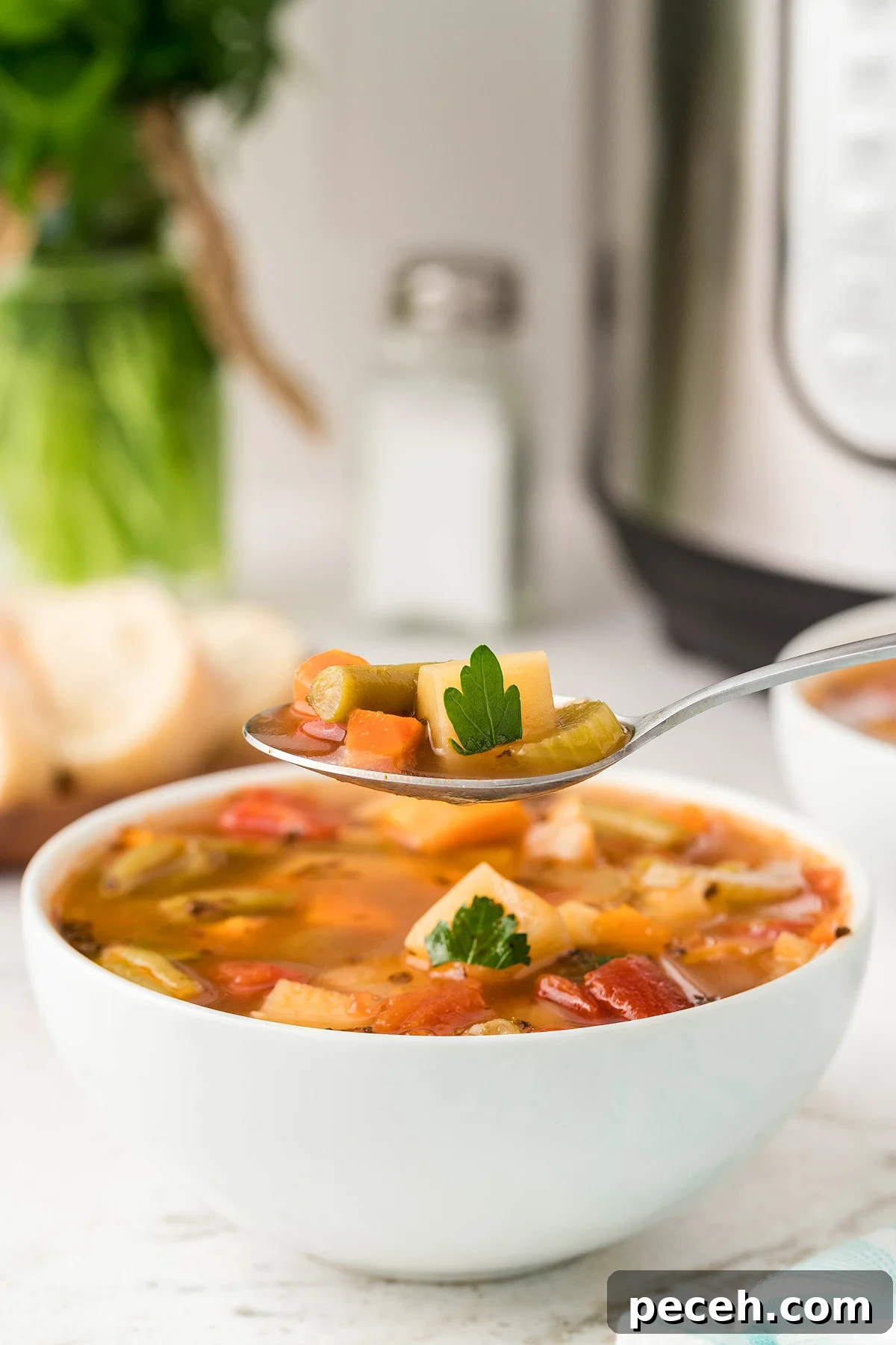 A spoonful of Instant Pot Vegetable Soup held above a bowl, with parsley garnish and bread in the background—an inviting vegetarian or vegan soup recipe using fresh and frozen vegetables.