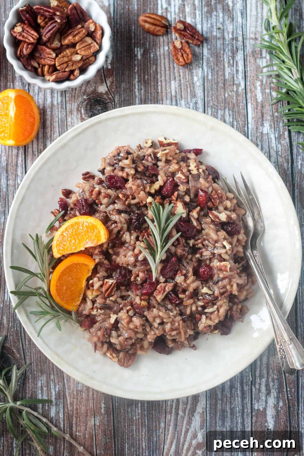 Cranberry Pecan Wild Rice Salad: a nutty, chewy wild rice blended with sweet-tart cranberries and buttery pecans — ideal for holidays or a filling lunch. Thanksgiving rice with cranberries, citrus, and rosemary on a cream colored plate.