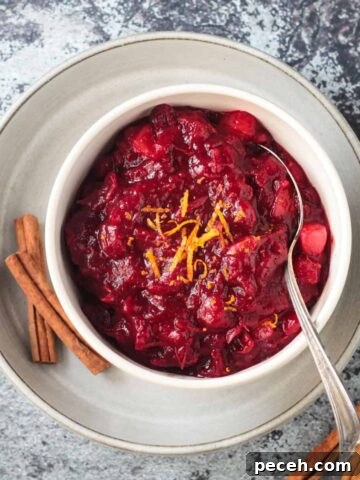 Cranberry sauce in a white bowl on a white plate with 2 cinnamon sticks.