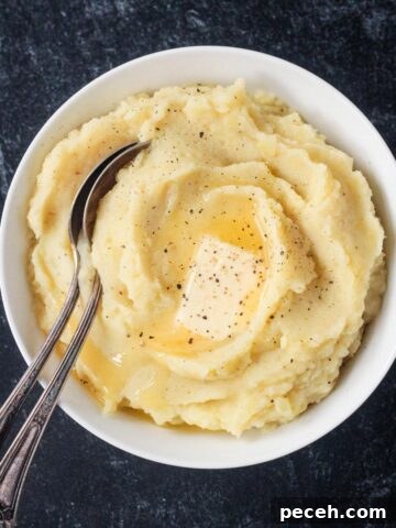 Serving spoon in a bowl of creamy mashed potatoes topped with a pat of butter.