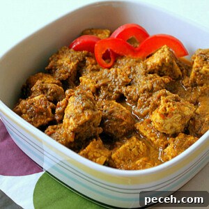 A spinach tomato curry in a white bowl with red pepper garnish