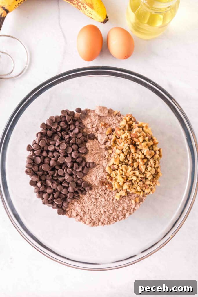 Glass mixing bowl with brownie mix, chocolate chips, and chopped walnuts on a marble countertop.