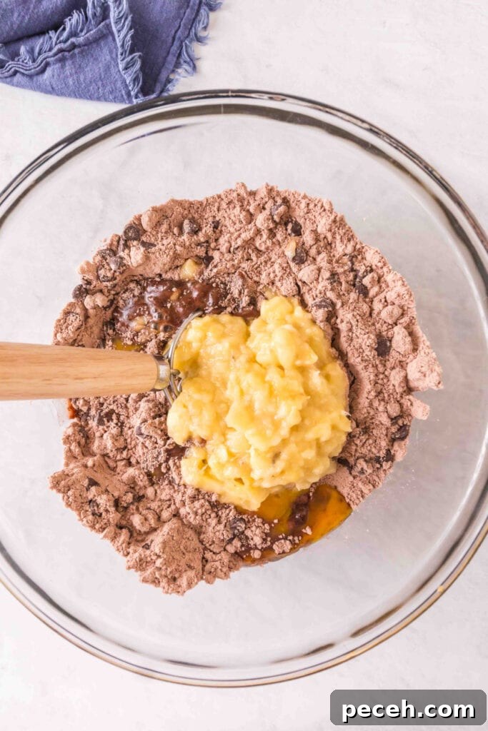 Mixing bowl with brownie mix, chocolate chips, walnuts, eggs, oil, and mashed bananas being added.