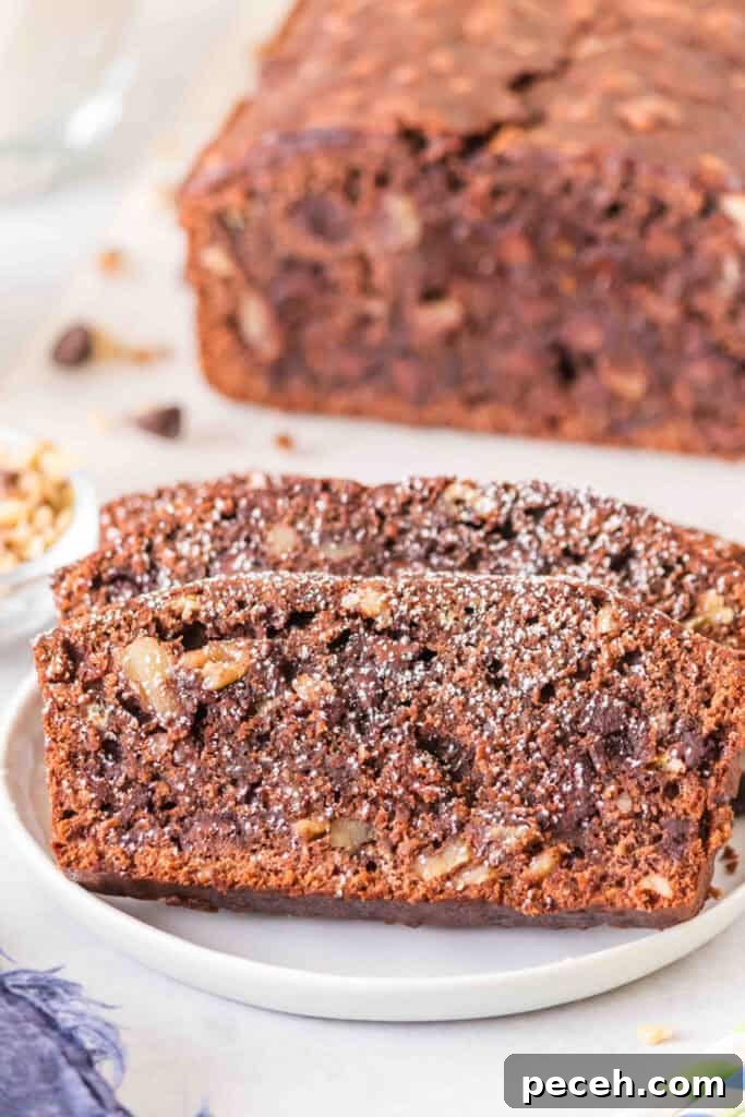 Close up of sliced brownie banana bread dusted with powdered sugar on a white plate with a loaf in the background.