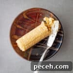 A roll of homemade miso butter on a small brown dish with a small butter knife to the side.