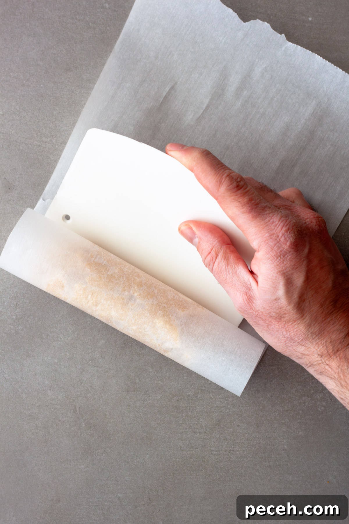 Savory Miso Butter Recipe for Bread, Veggies, and Steak 7 A hand pushing a bench scraper against a roll of miso butter in parchment paper.