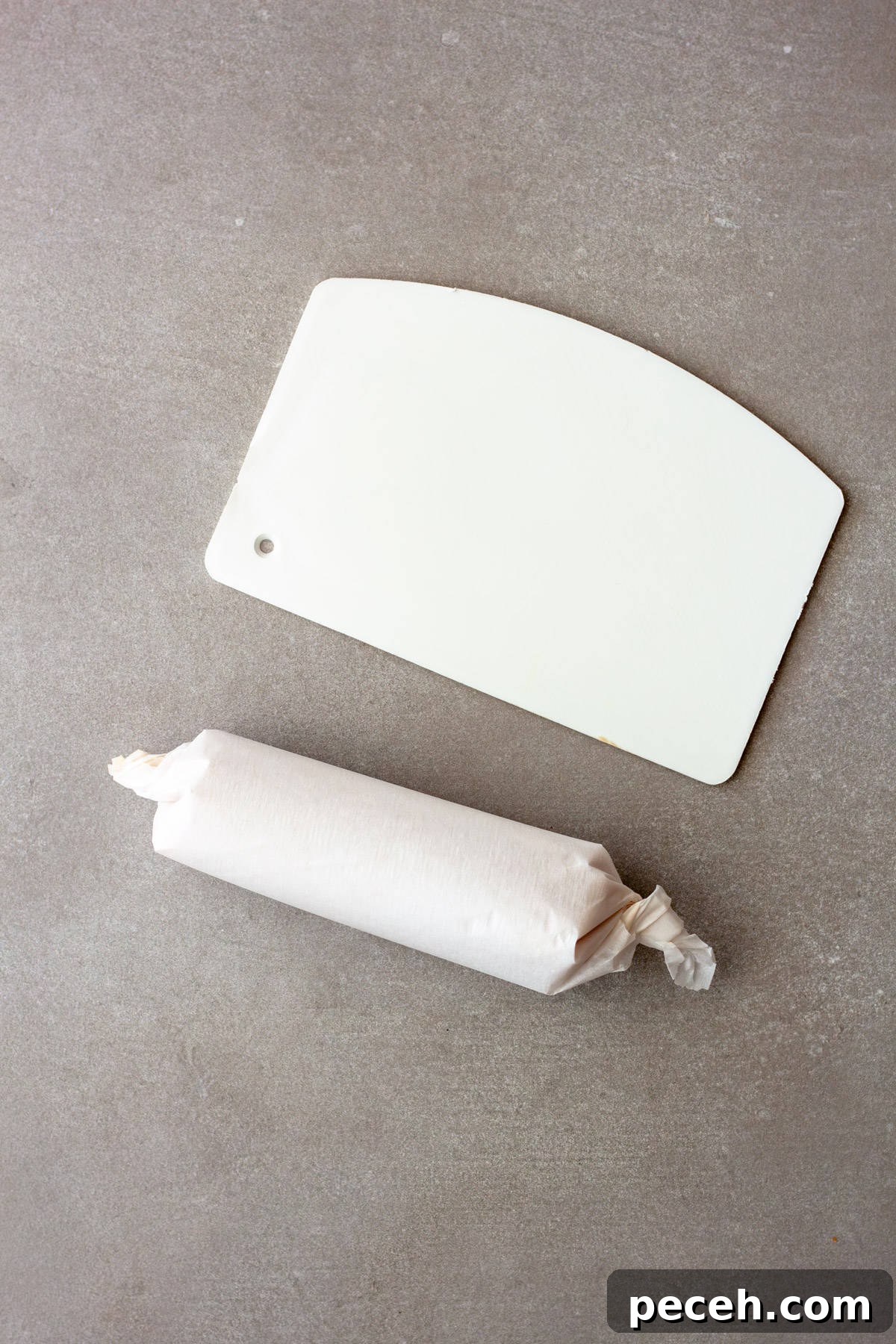 Savory Miso Butter Recipe for Bread, Veggies, and Steak 8 A roll of miso butter in parchment paper and a white bench scraper on a gray table.