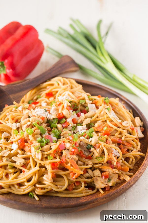 Spicy Peanut Chicken Noodles Recipe for Quick Weeknight Meals 4 Easy Spicy Peanut Noodles With Chicken on a wood serving plate with a wood serving spoon, and a whole red pepper and a bundle of green onions in the background.