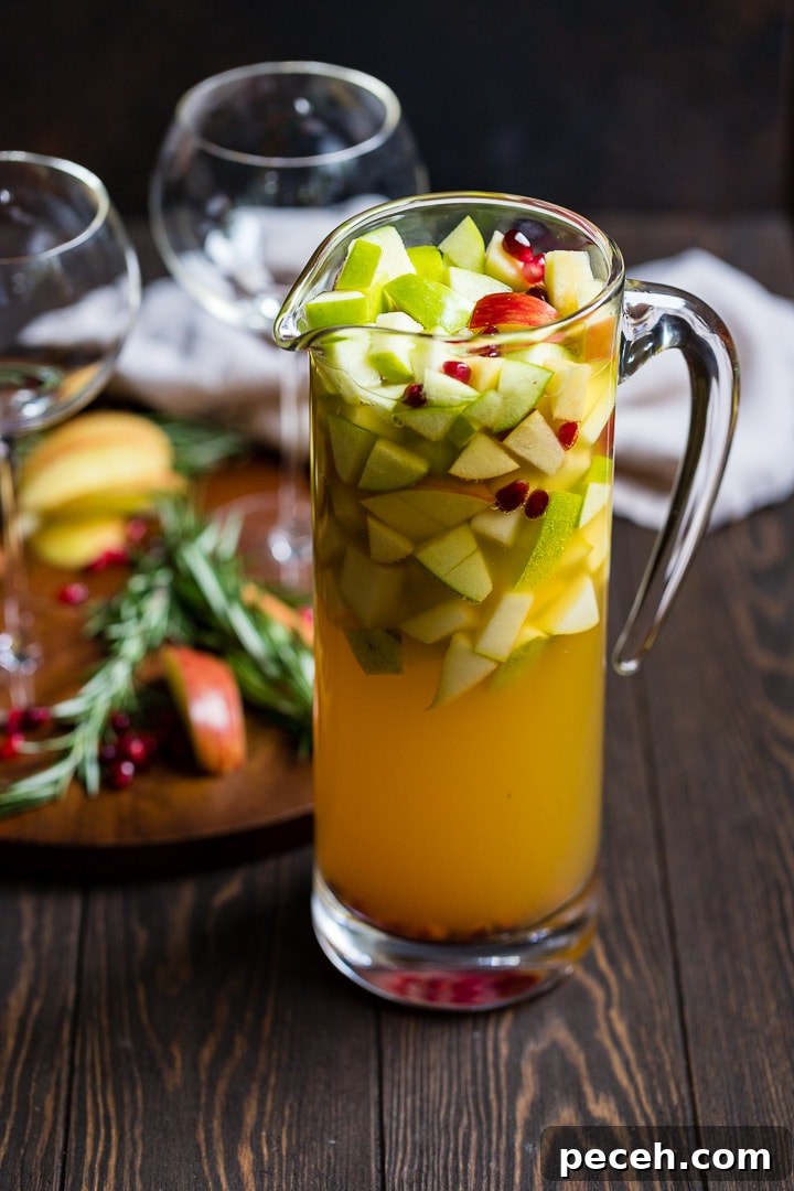 Autumn Harvest White Sangria Recipe for Cozy Fall Gatherings 3 Large pitcher of autumn harvest white sangria with apples, pears, white wine, apple cider, and pomegranate seeds.