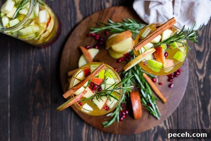 Autumn Harvest White Sangria Recipe for Cozy Fall Gatherings 5 Overhead shot of two glasses filled with autumn harvest white sangria, garnished with rosemary and cinnamon sticks.