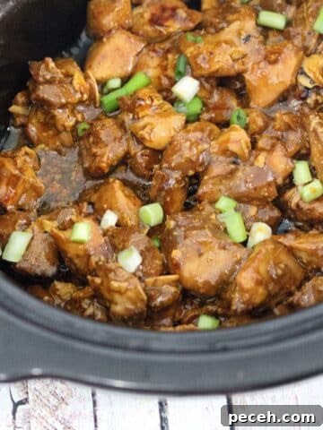 Black slow cooker with teriyaki chicken being scooped by yellow tongs and topped with green onions