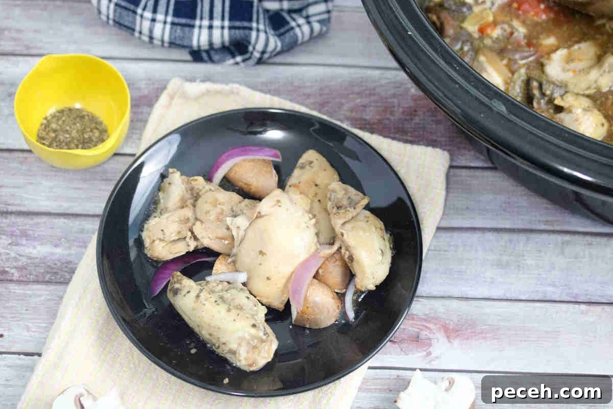 Hunters chicken thighs on a black plate with red onions on it and a slow cooker behind it.