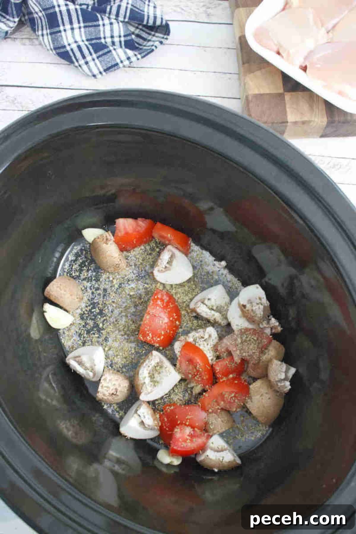 Black slow cooker with mushrooms, tomatoes, and seasoning in it.