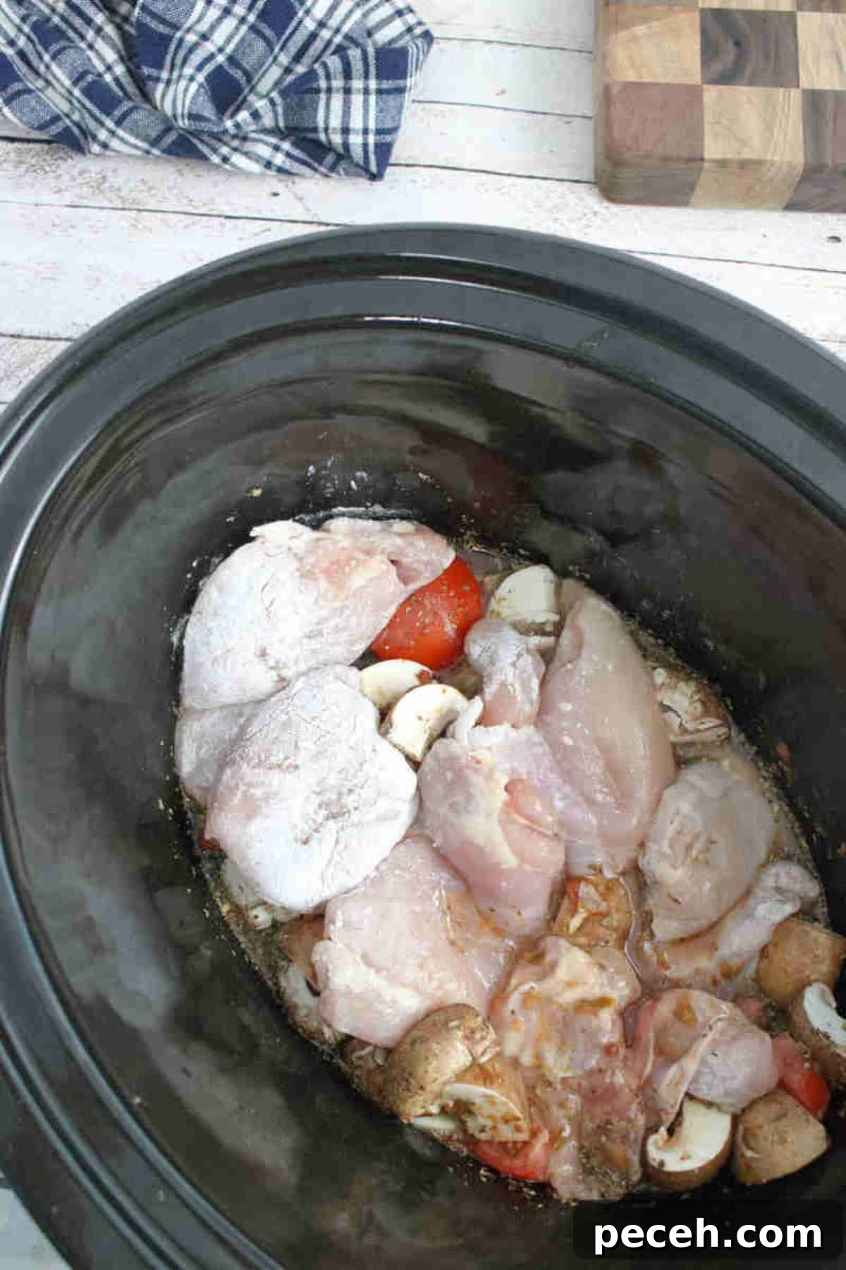 Raw chicken in a slow cooker with mushrooms, tomatoes and broth.