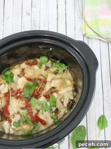 Pin image with text: black slow cooker with dairy-free tuscan chicken, sauce, sundried tomatoes and basil with the lid on a colored linen beside it