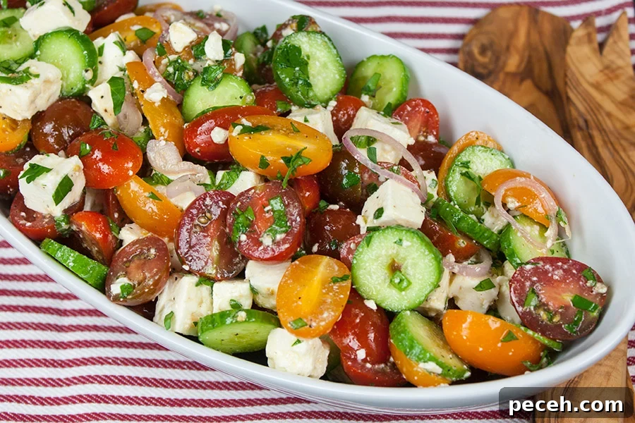 Tomato Cucumber Feta Salad in a white serving bowl on a red striped tablecloth.
