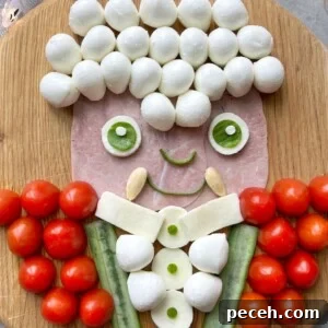 Halloween Charcuterie Board Ideas for a Spooky Party 4 A playful food art portrait of a Vampire on a wooden board, using mozzarella balls for hair, ham for the face, cucumber and mozzarella for the body. His red jacket is made of cherry tomatoes.